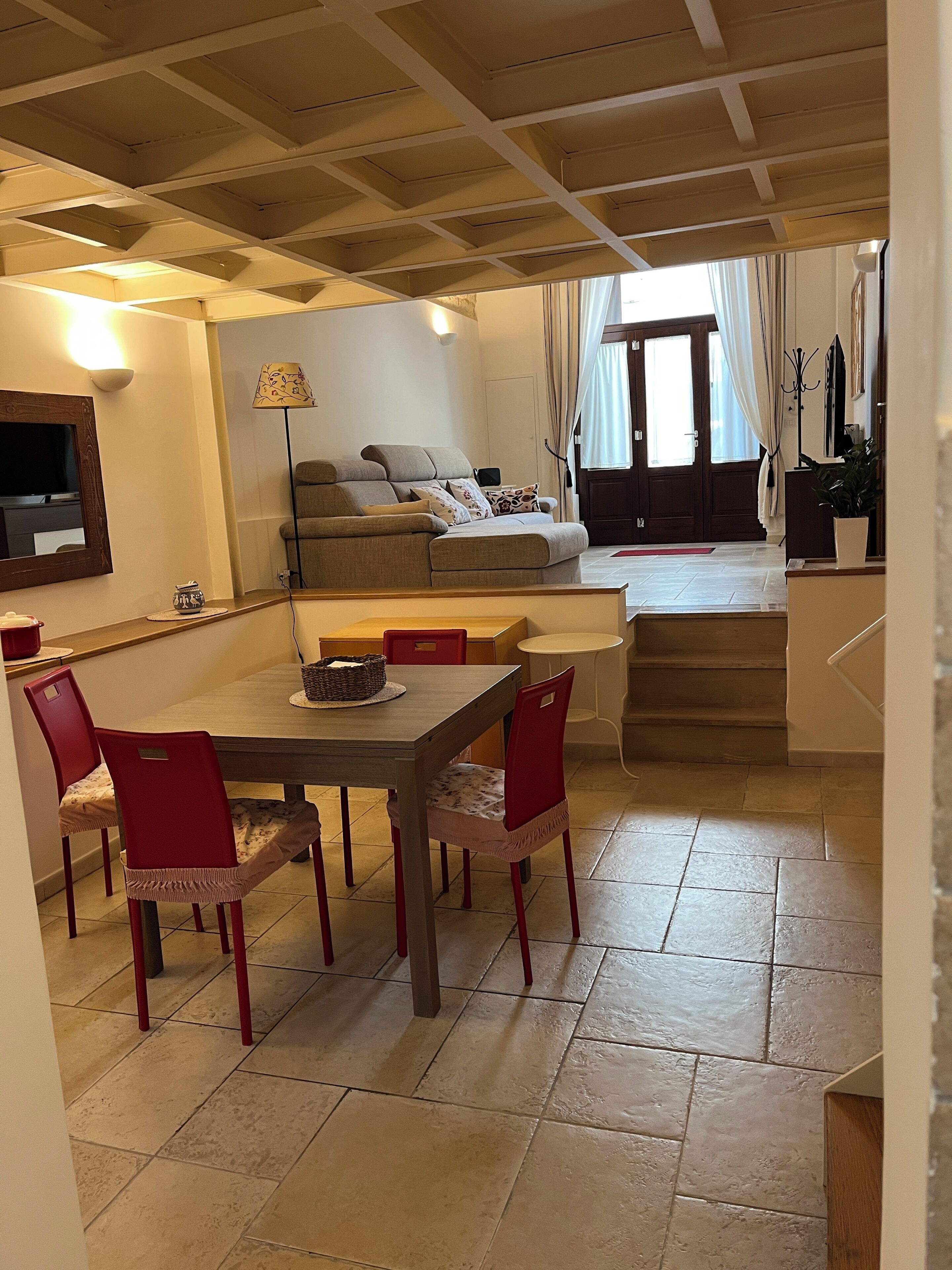 Zona pranzo con tavolo e sedie, un divano, una TV e una scala che porta a un piano superiore.