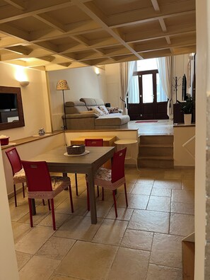 A dining area with a table and chairs, a sofa, a TV, and a staircase leading to an upper level. - Vrbo Property (Mola di Bari)