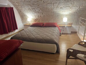 Een kamer met een bed, een stoel, een tafeltje en een stenen muur.
