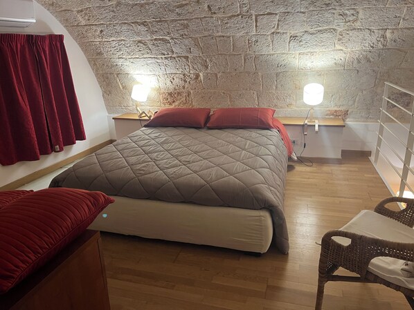 A room with a bed, a chair, a small table, and a stone wall. - Vrbo Property (Mola di Bari)
