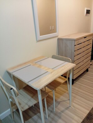 Une petite pièce, bien rangée, avec une table en bois, deux chaises, un miroir et une commode en bois.