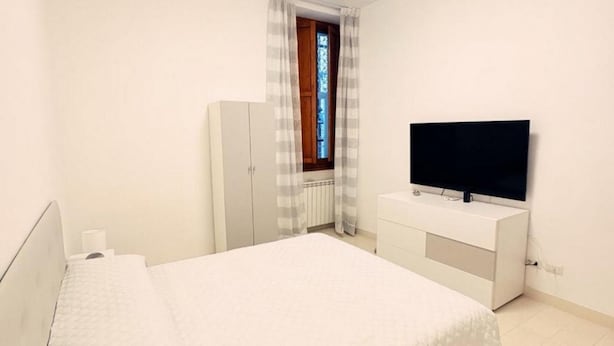 Um quarto com uma cama, um guarda-roupa, uma televisão e uma janela com cortinas.