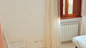 Um quarto com cama, radiador, janela com persianas de madeira e uma cadeira.