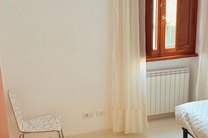 Ein Zimmer mit einem Bett, einem Heizkörper, einem Fenster mit Holzläden und einem Sessel.