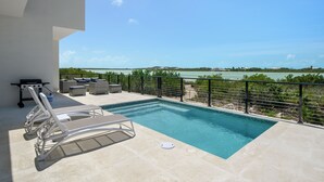 A pool with lounge chairs, a grill, and a view of the sea. - Spacious 4-bedroom house with Gorgeous Views from Every Room (Venetian Road)