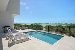 A pool with lounge chairs, a grill, and a view of the sea. - Spacious 4-bedroom house with Gorgeous Views from Every Room (Venetian Road)
