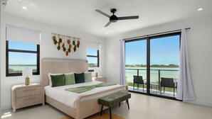 A bedroom with a bed, bedside tables, a ceiling fan, a view of the sea, and a balcony with chairs. - Spacious 4-bedroom house with Gorgeous Views from Every Room (Venetian Road)