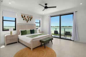 A bedroom with a bed, bedside tables, a ceiling fan, a view of the sea, and a balcony with chairs. - Spacious 4-bedroom house with Gorgeous Views from Every Room (Venetian Road)