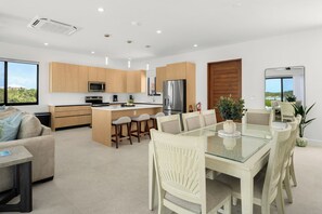 A modern kitchen with wooden cabinets, a central island with seating, and a dining area with a glass table and chairs. - Spacious 4-bedroom house with Gorgeous Views from Every Room (Venetian Road)