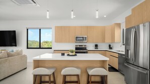 A modern kitchen with wooden cabinets, a central island with stools, a stainless steel refrigerator, and a flat-screen TV mounted on the wall. - Spacious 4-bedroom house with Gorgeous Views from Every Room (Venetian Road)