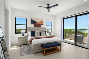 A bedroom with a large bed, nightstands, a bench, a ceiling fan, and a balcony with outdoor furniture. - Spacious 4-bedroom house with Gorgeous Views from Every Room (Venetian Road)