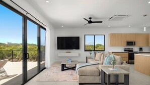 A modern living room with a sofa, coffee table, and TV, a kitchen with wooden cabinets, and a balcony with a view. - Spacious 4-bedroom house with Gorgeous Views from Every Room (Venetian Road)
