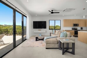 A modern living room with a sofa, coffee table, and TV, a kitchen with wooden cabinets, and a balcony with a view. - Spacious 4-bedroom house with Gorgeous Views from Every Room (Venetian Road)