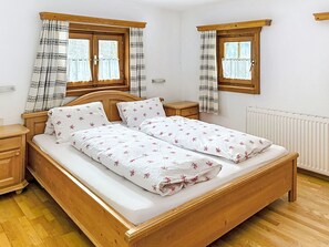 A double bed with floral bedding, wooden headboard, two bedside tables, and curtains on windows.