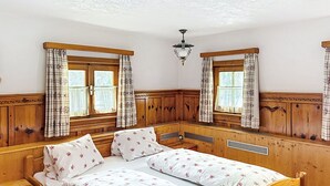 A wooden room with a bed, two windows with curtains, a ceiling light, and a wooden bench.