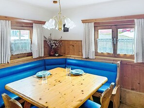 A corner seating area with a wooden table, blue cushioned benches, and a chandelier.