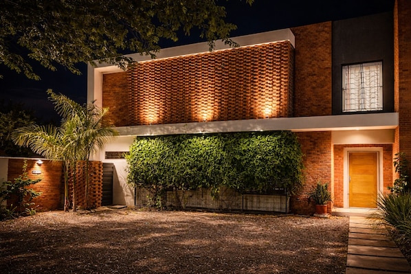 A modern two-story building with a brick facade, a green climbing wall, and a well-lit entrance.