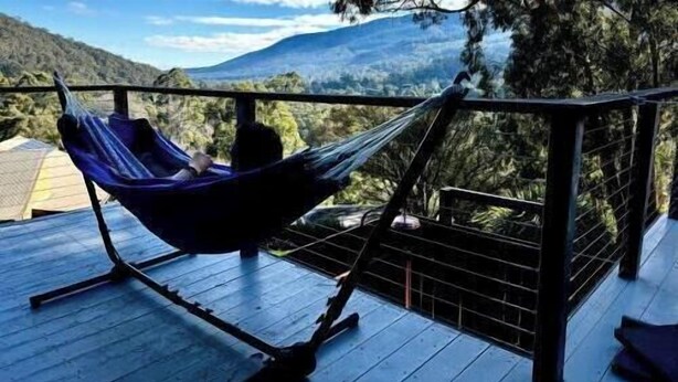 Una hamaca sobre una terraza de madera con vistas a una montaña y árboles.