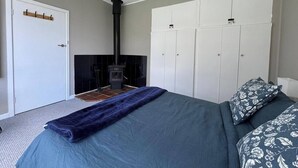 Un dormitorio con cama, armario, chimenea y un perchero junto a la puerta.