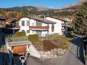 Un bâtiment moderne à deux étages, doté d’un garage, d’une terrasse en bois et d’un chemin de pierre menant à une borne d’incendie bleue.