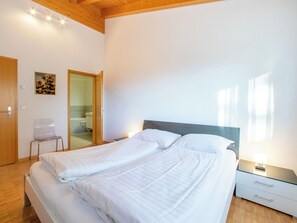 Une chambre à coucher comprenant un lit, une table de chevet, une chaise et une porte donnant sur une salle de bain.