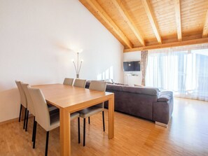 Un espace de vie moderne comprenant une table à manger en bois, des chaises, un canapé et un téléviseur fixé au mur.