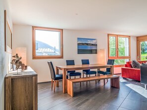 Ein modernes Zimmer mit einem Holzesstisch, blauen Stühlen, einem roten Sofa und großen Fenstern mit Blick ins Freie.