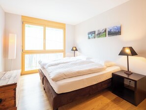 A bedroom with a bed, two bedside lamps, a wooden nightstand, a window, and three wall-mounted pictures. - Cosy apartment for 6 people with WIFI, TV and terrace (Waldhaus)