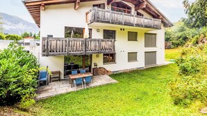 Un chalet à deux étages doté d’un balcon en bois, d’une terrasse avec des meubles d’extérieur et offrant une vue sur les montagnes.