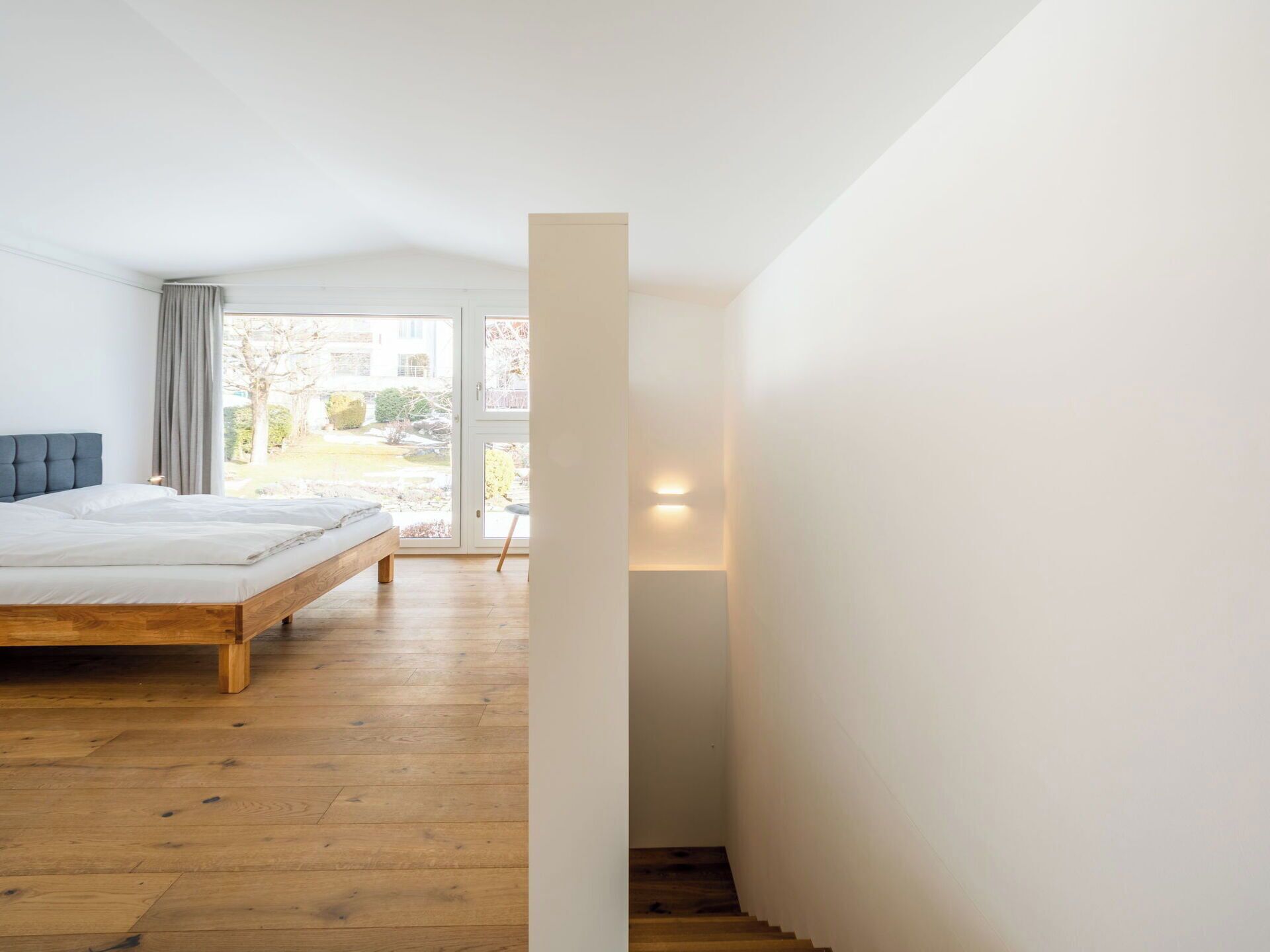 Un dormitorio con una cama de madera, vistas a través de un ventanal y una escalera.