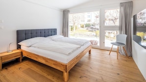 Una camera da letto con un letto di legno, un comodino, una sedia e un'ampia finestra con tende.