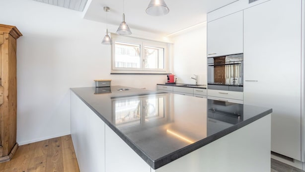 Una cucina moderna con una grande isola centrale, luci a sospensione e mobili bianchi.