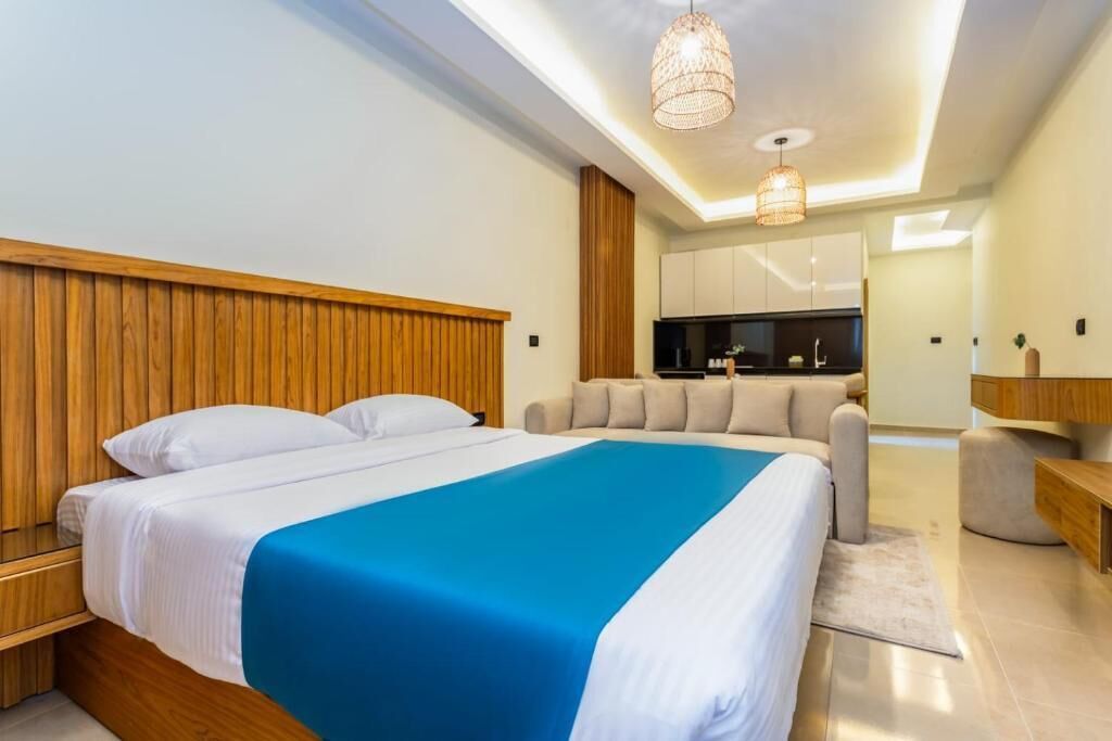 Ein modernes Schlafzimmer mit einem großen Bett, einem Holzkopfstück und einer kleinen Küchenzeile im Hintergrund.