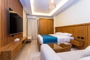 Ein Hotelzimmer mit Fernseher, einem Bett mit blauen Akzenten, einem Holzkopfende, einem Nachttisch und einer Couch.
