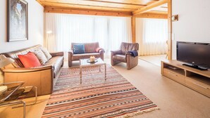 Ein Wohnzimmer mit einer Couch, zwei Sesseln, einem Couchtisch, einem Fernseher und einem gemusterten Teppich.