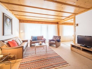 Ein Wohnzimmer mit einer Couch, zwei Sesseln, einem Couchtisch, einem Fernseher und einem gemusterten Teppich.