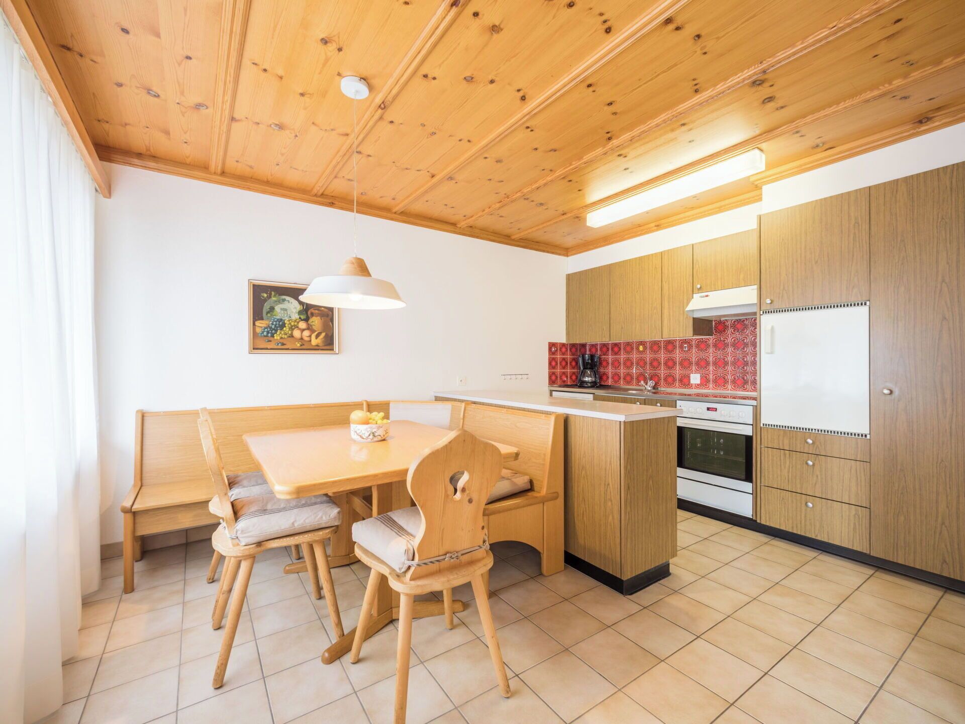 Une cuisine de taille réduite avec des meubles en bois, un coin repas comprenant un banc et des chaises, et un sol carrelé.