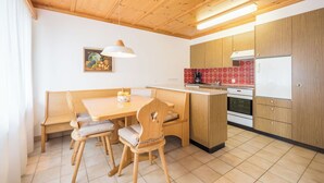 Eine kleine Küche mit Holzausstattung, ein Essbereich mit einer Bank und Stühlen sowie ein Fliesenboden.