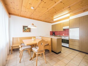 Una cocina compacta con armarios de madera, una zona de comedor con un banco y sillas, y piso de baldosas.