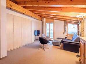 Een kamer met een houten plafond, een televisie, een bank, een stoel en een raam met uitzicht.