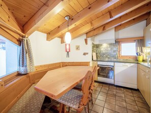 Una mesa de comedor de madera con sillas, una cocina con estufa y lavavajillas, y un ventanal con cortinas.