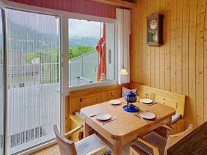 A wooden dining area with a table set for two, a window with curtains, and a wall clock. - Cosy apartment for 4 guests with WIFI, TV, terrace, pets allowed and panoramic view (Sagogn)