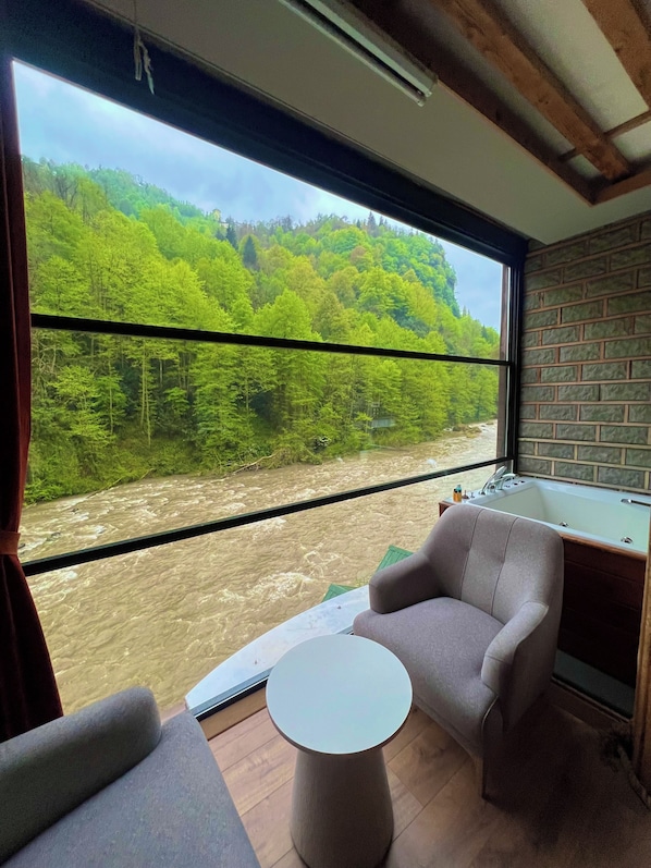 Una habitación con un gran ventanal, una bañera, una mesa redonda y un sofá.