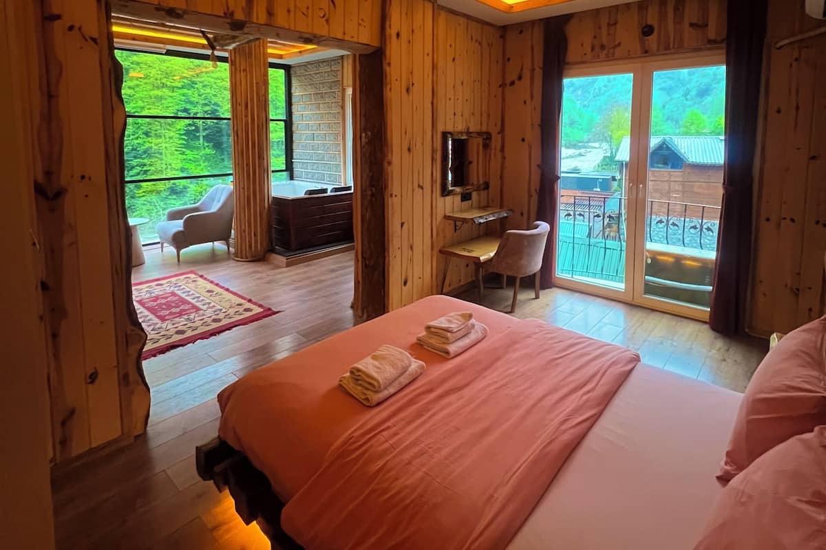 A wooden room with a bed, a desk, and a view of greenery outside.