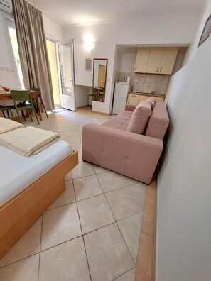 A hotel room with a bed, a pink sofa, a small kitchen area, and a dining table with chairs. - One bedroom apartment with terrace (Neum)