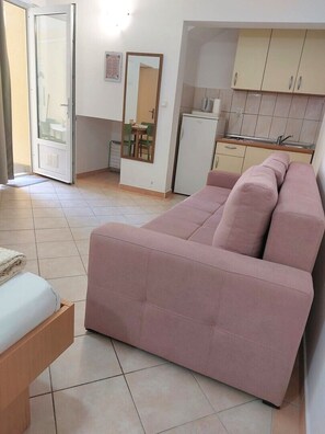 A room with a sofa, a small table, a kitchenette, and a door. - One bedroom apartment with terrace (Neum)