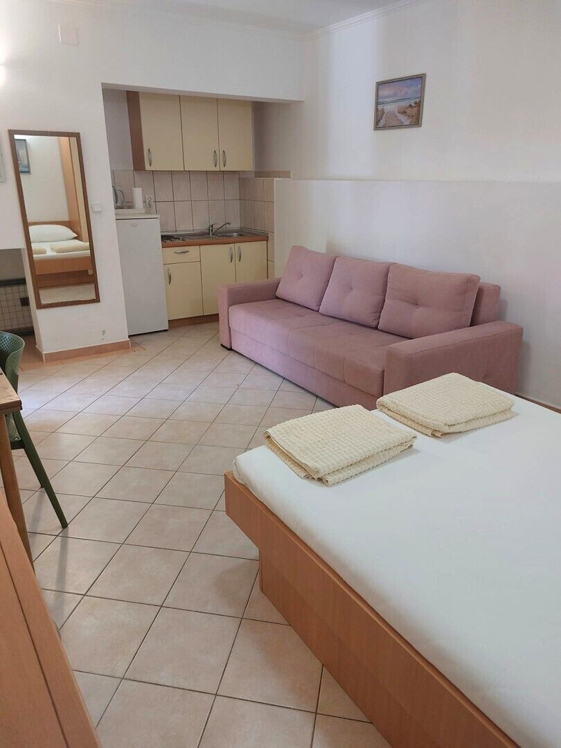 Une chambre avec un lit, un canapé rose, une petite kitchenette et un miroir.