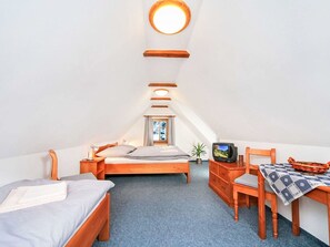Et hyggeligt, godt oplyst soveværelse på loftet med seng, skrivebord, stol og fjernsyn.