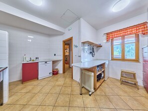 Eine Küche mit weißen Fliesen, einem roten Schrank, einem Geschirrspüler, einer Heizung und einem Fenster mit einem karierten Vorhang.