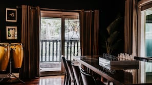 Una habitación con una mesa de comedor, sillas, un tablero de ajedrez, un set de batería y una planta grande.